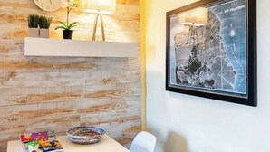 A dining area with a wooden wall, a clock, a lamp, a framed map, and a table with snacks and a bowl. - Walkable Urban Retreat - 2 En-Suite Baths - Near Top Dining & Shops & Hotspots! (SF)