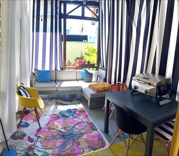 A patio with a sofa, chairs, a grill, and a colorful rug.
