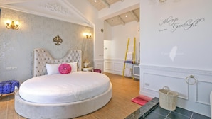 Un dormitorio espacioso con una cama redonda grande, un muro decorativo con un cartel que dice 'Always Goodnight kiss me', y un techo de madera.