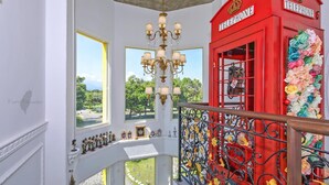 Una cabina telefónica roja con decoración floral, un candelabro y una barandilla de balcón con flores.