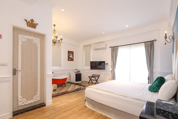 A hotel room with a large bed, a TV, a small desk, a red bathtub, and a chandelier. - Shanti B&B (Luodong)