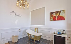 A bathroom with a freestanding bathtub, a wall-mounted sink, a refrigerator, and a painting. - Shanti B&B (Luodong)