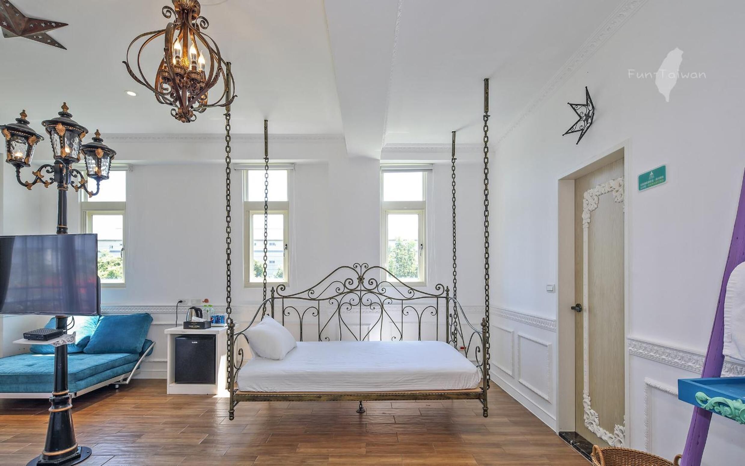A spacious bedroom with a four-poster bed, a chandelier, and a view of the outdoors through large windows.
