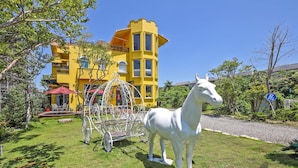 Una estatua de un caballo blanco en un área verde, con un edificio amarillo al fondo.