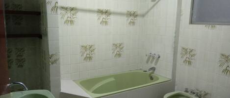 Un baño con una bañera verde, un lavamanos blanco y un bidé. Las paredes presentan un diseño con palmeras.