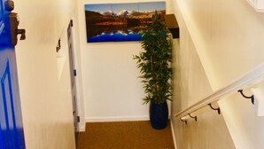 A staircase with a wooden handrail, a potted plant, and a framed landscape painting on the wall.
