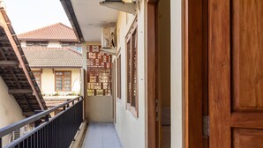 Een smalle gang met een houten deur aan de rechterkant, een betegelde vloer en een balkon met een leuning aan de linkerkant.