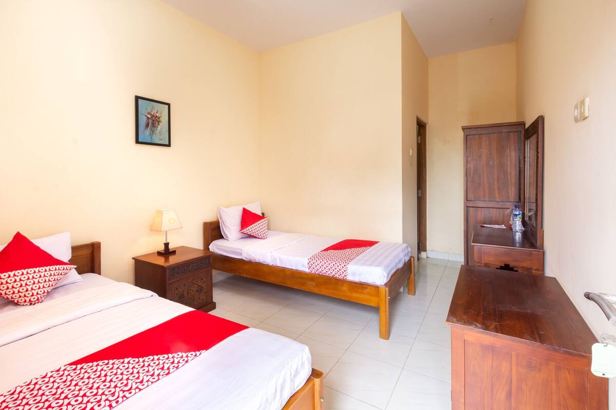 Een hotelkamer met twee bedden, een houten dressoir, een spiegel en een ingelijst schilderij aan de muur.
