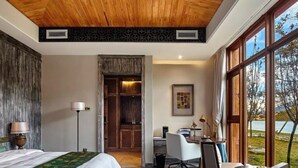Ett hotellrum med ett träpanelat tak, en säng med ett grönt och vitt överkast, ett skrivbord med en stol och ett stort fönster med utsikt över omgivningarna.