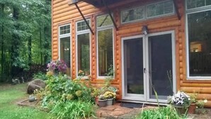 Une cabane en rondins avec un chemin de pierres menant à l’entrée, entourée d’une végétation luxuriante et de plantes en pot.