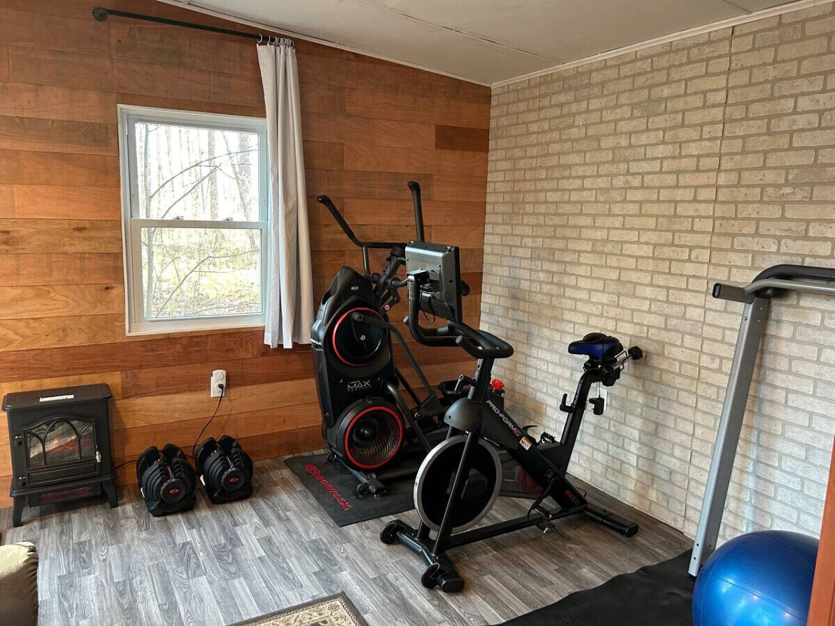 A gym with a stationary bike, elliptical, and weights.