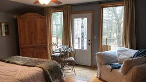 Une chambre avec deux lits, une armoire en bois, une table à manger avec des chaises, un canapé et un balcon avec des rideaux.