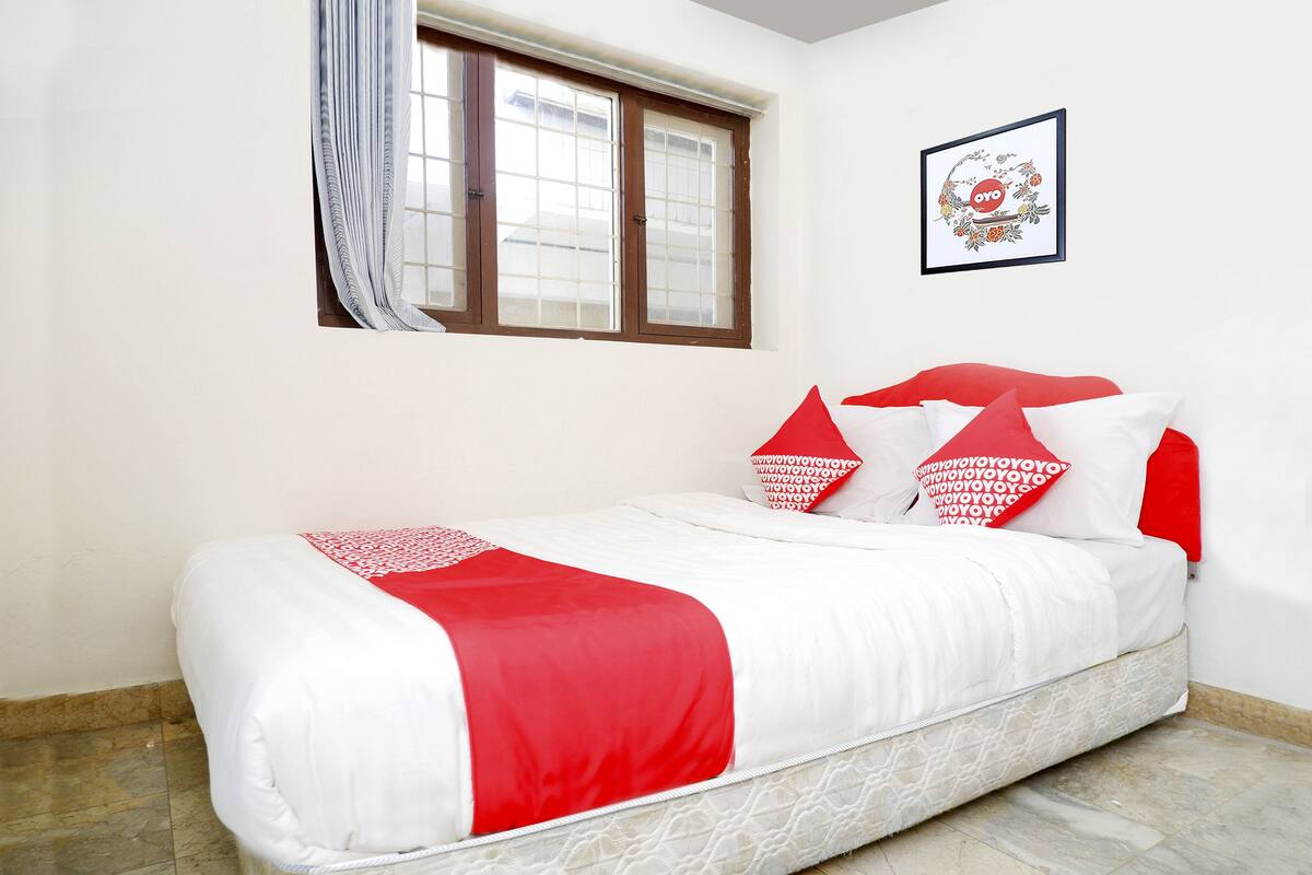Ein Bett mit weißer und roter Bettwäsche, ein Fenster mit Vorhängen und ein gerahmtes Bild an der Wand.