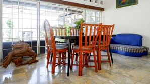 A dining area with a table and chairs, a blue sofa, and a large window with a view of the outside. - OYO 1196 Hotel Pura Puspa Rosa (Depok)