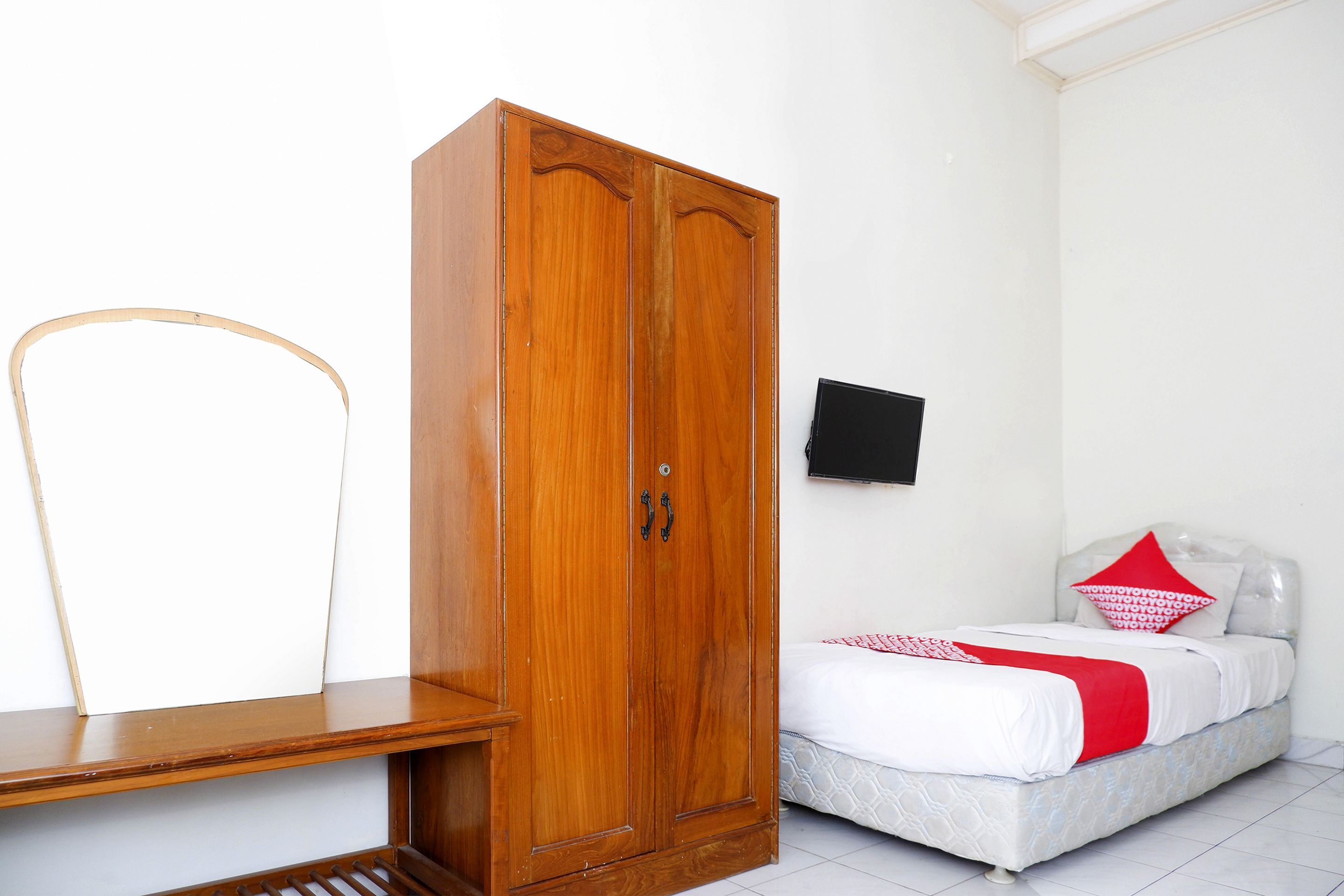 Ein Schlafzimmer mit einem Holzschrank, einem Bett mit rotem und weißem Überwurf und einem an der Wand befestigten Fernseher.