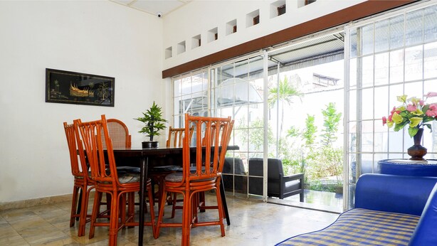 A dining area with a table and chairs, a potted plant, and a sofa with a patterned cushion. - OYO 1196 Hotel Pura Puspa Rosa (Depok)