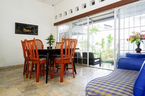 Un coin repas avec une table et des chaises, une plante en pot et un canapé agrémenté d’un coussin à motifs.