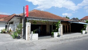 A building with a tiled roof, a covered entrance, and potted plants around the entrance. - OYO 1196 Hotel Pura Puspa Rosa (Depok)
