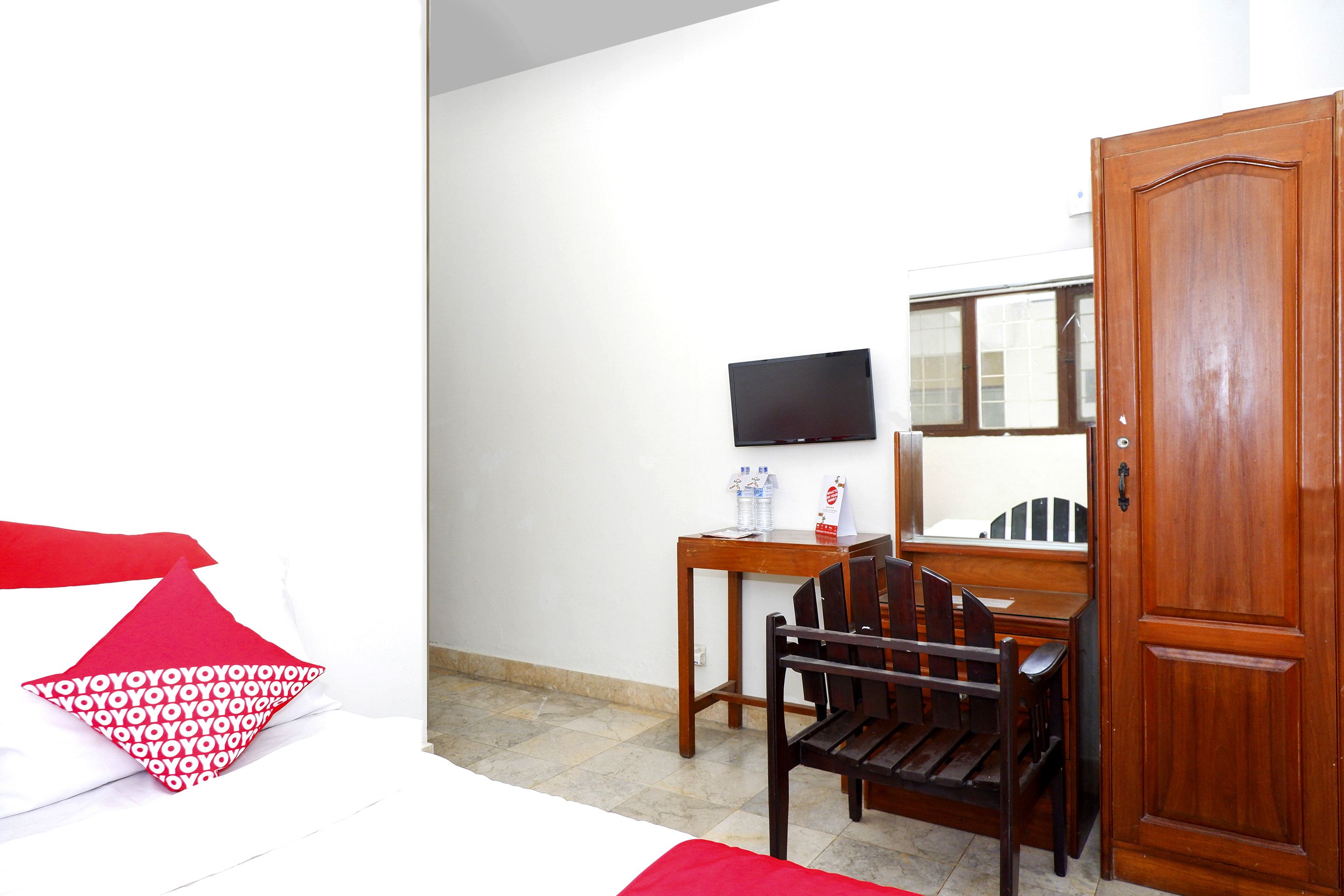 A hotel room with a bed, a wooden desk, a chair, a television, and a wardrobe.