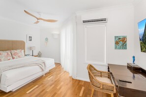 Et soveværelse med seng, skrivebord, stol, loftventilator og kunst på væggen.