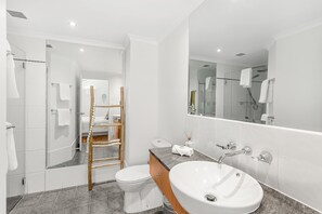 Et moderne badeværelse med toilet, vask og glasvæg omkring brusebadet.