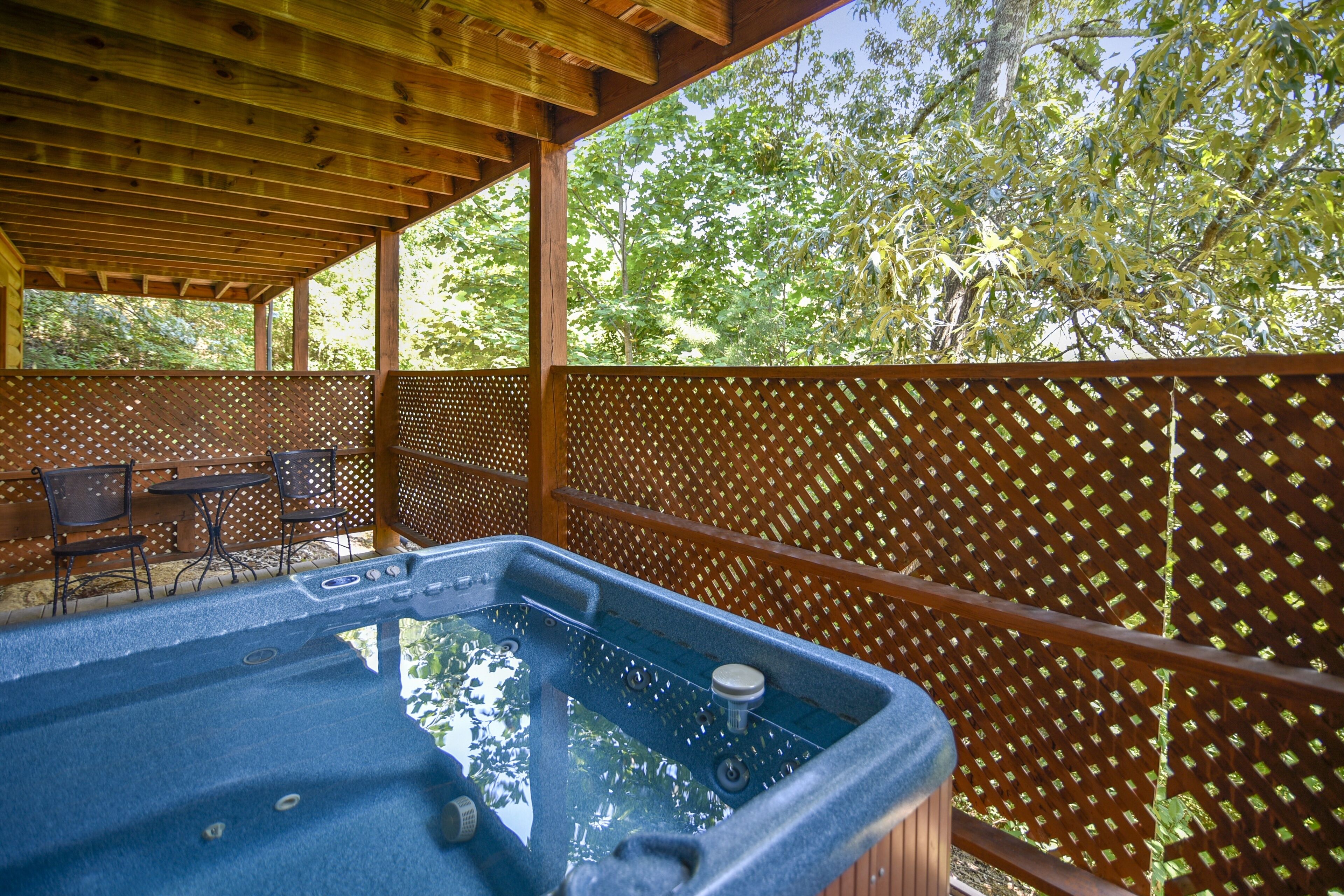 A hot tub under a wooden pergola with a view of trees.
