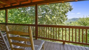 Eine Holzterrasse mit einem Holzstuhl, mit Blick auf eine bewaldete Gegend und freiem Ausblick auf die umliegende Landschaft.