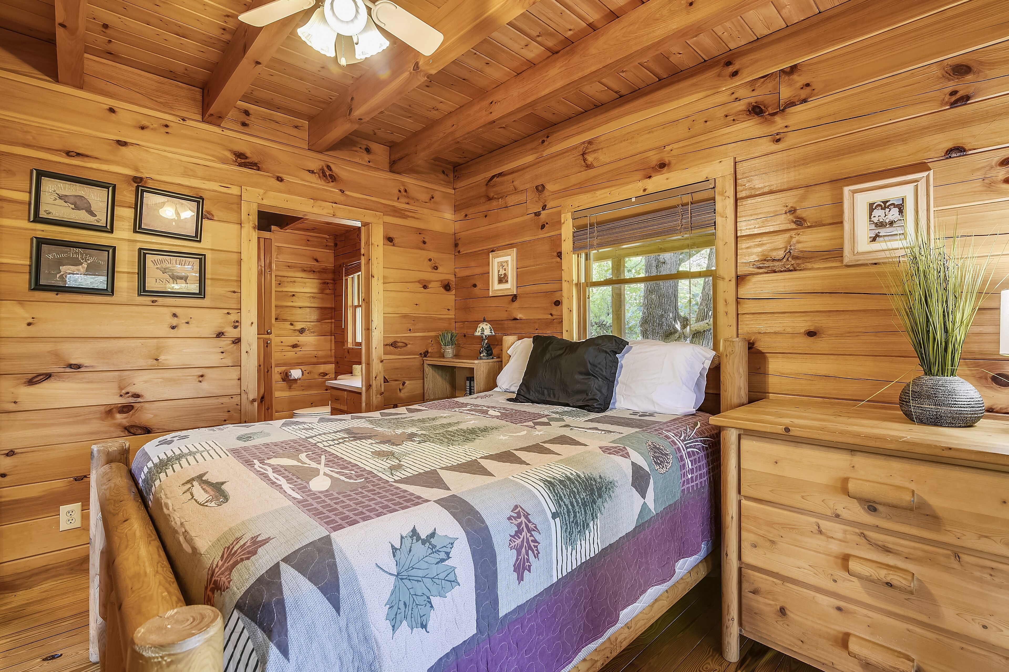 A wooden cabin bedroom with a bed, a nightstand, a dresser, and a window.