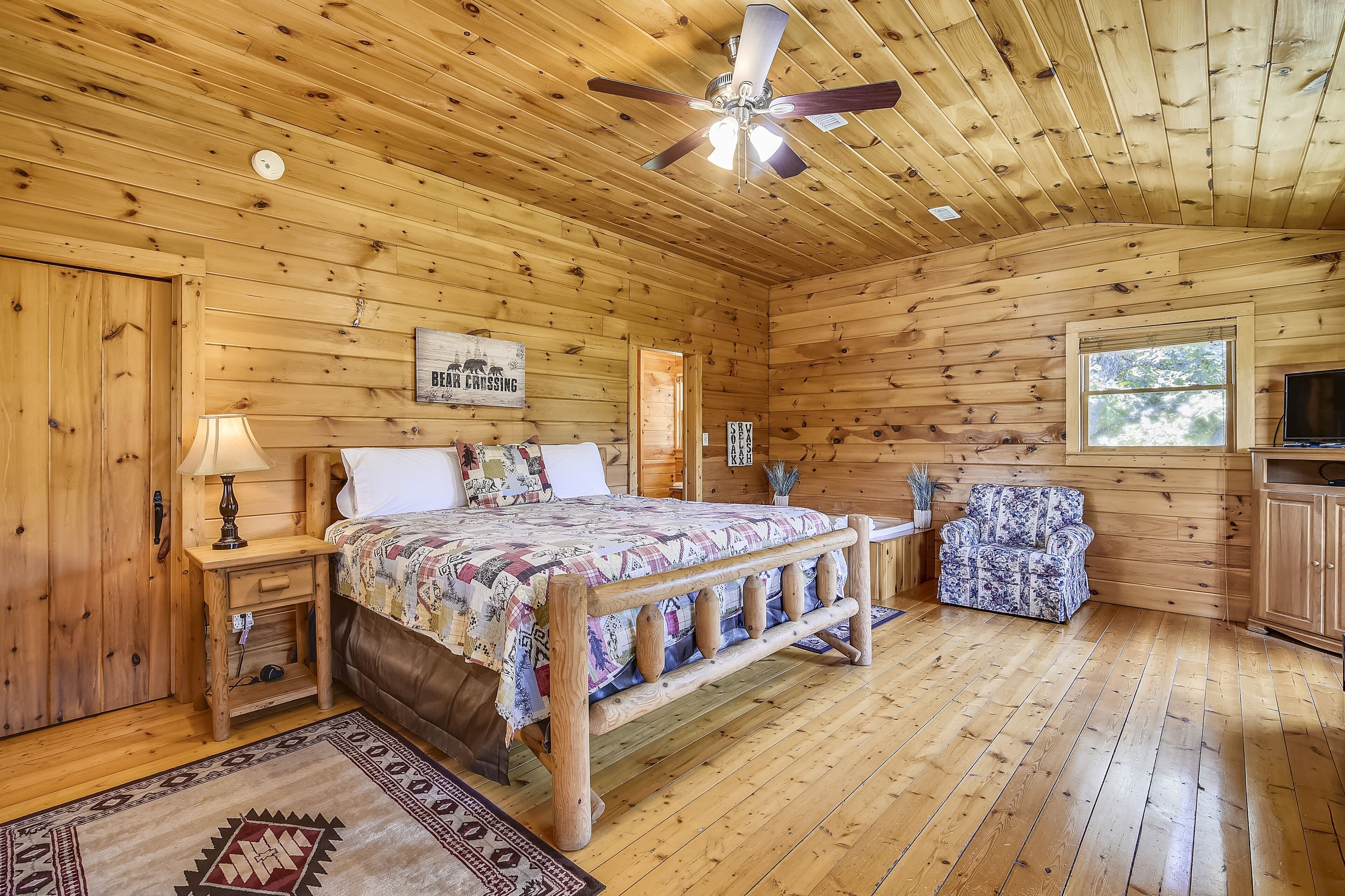 A wooden cabin bedroom with a bed, nightstand, lamp, and a ceiling fan.