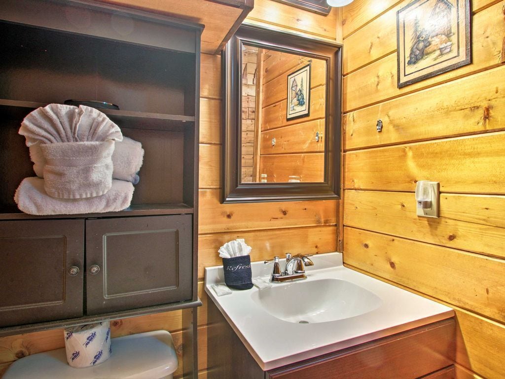 A wooden cabin bathroom with a sink, mirror, and towel storage.
