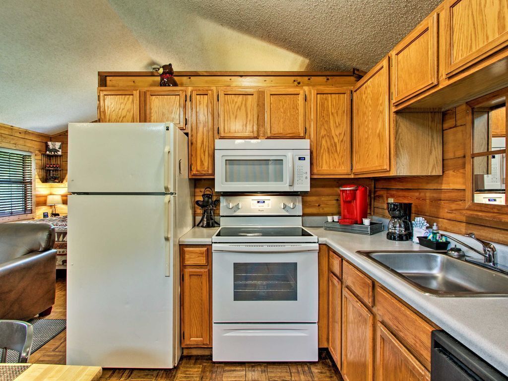 A compact kitchen with wooden cabinets, a refrigerator, a microwave, an oven, and a sink.