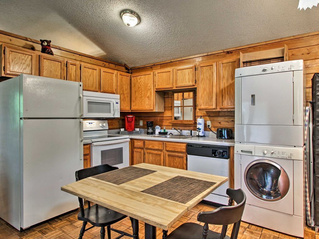 A compact kitchen with wooden cabinets, a microwave, a stove, a sink, a dishwasher, and a washing machine.