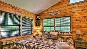 Un dormitorio tipo cabaña con una cama grande, paredes de madera y varias ventanas con persianas.