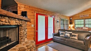 Interior acogedor de una cabaña con chimenea de piedra, un sofá de cuero con almohadones con motivos de osos y un cartel que indica el nombre de la cabaña.
