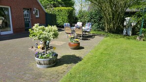 A courtyard with a brick building, outdoor seating, a large planter with flowers, and a lawn.