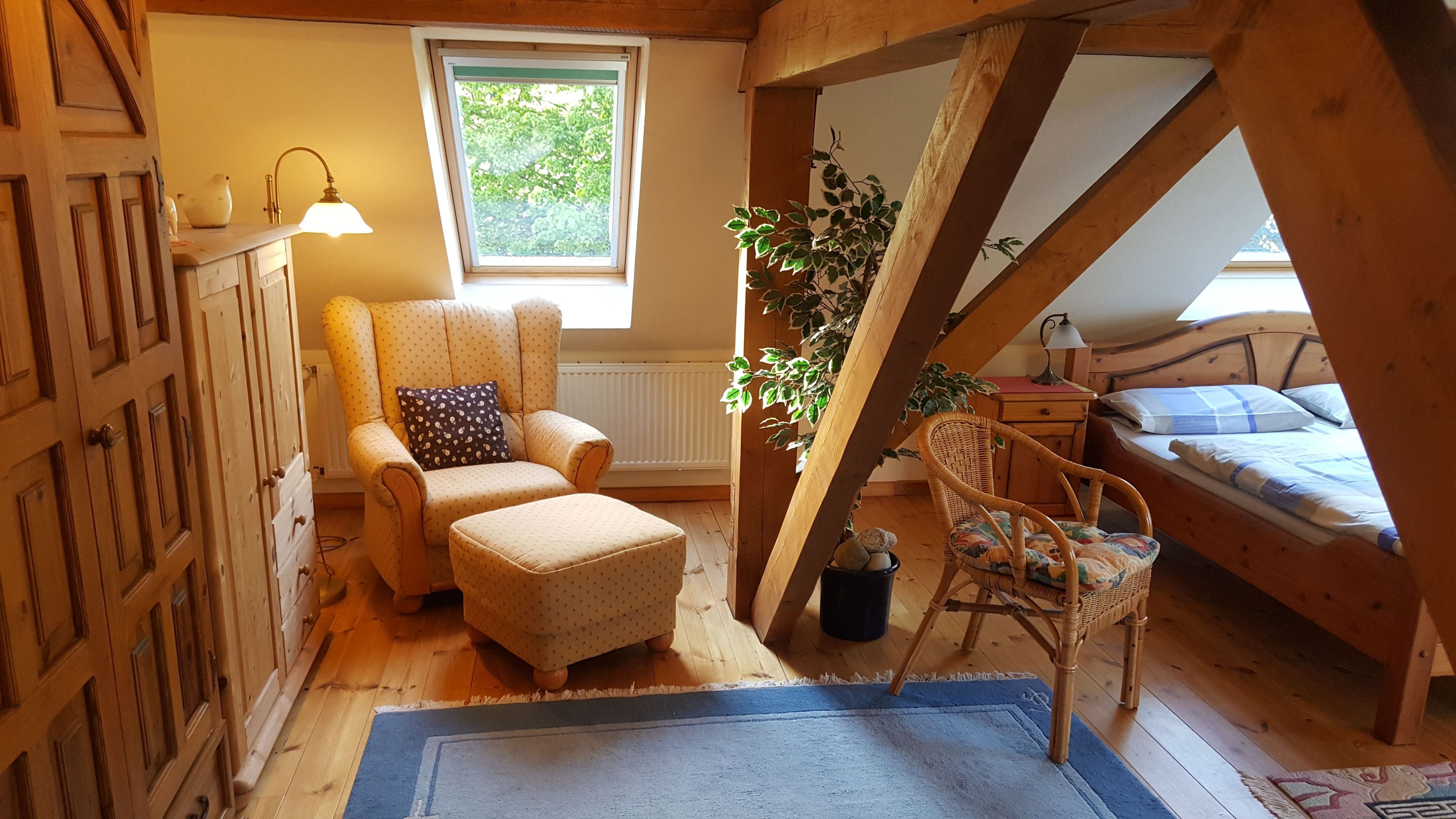 Une chambre mansardée chaleureuse avec un plafond en bois, une grande fenêtre, une chaise, un lit et une petite table.