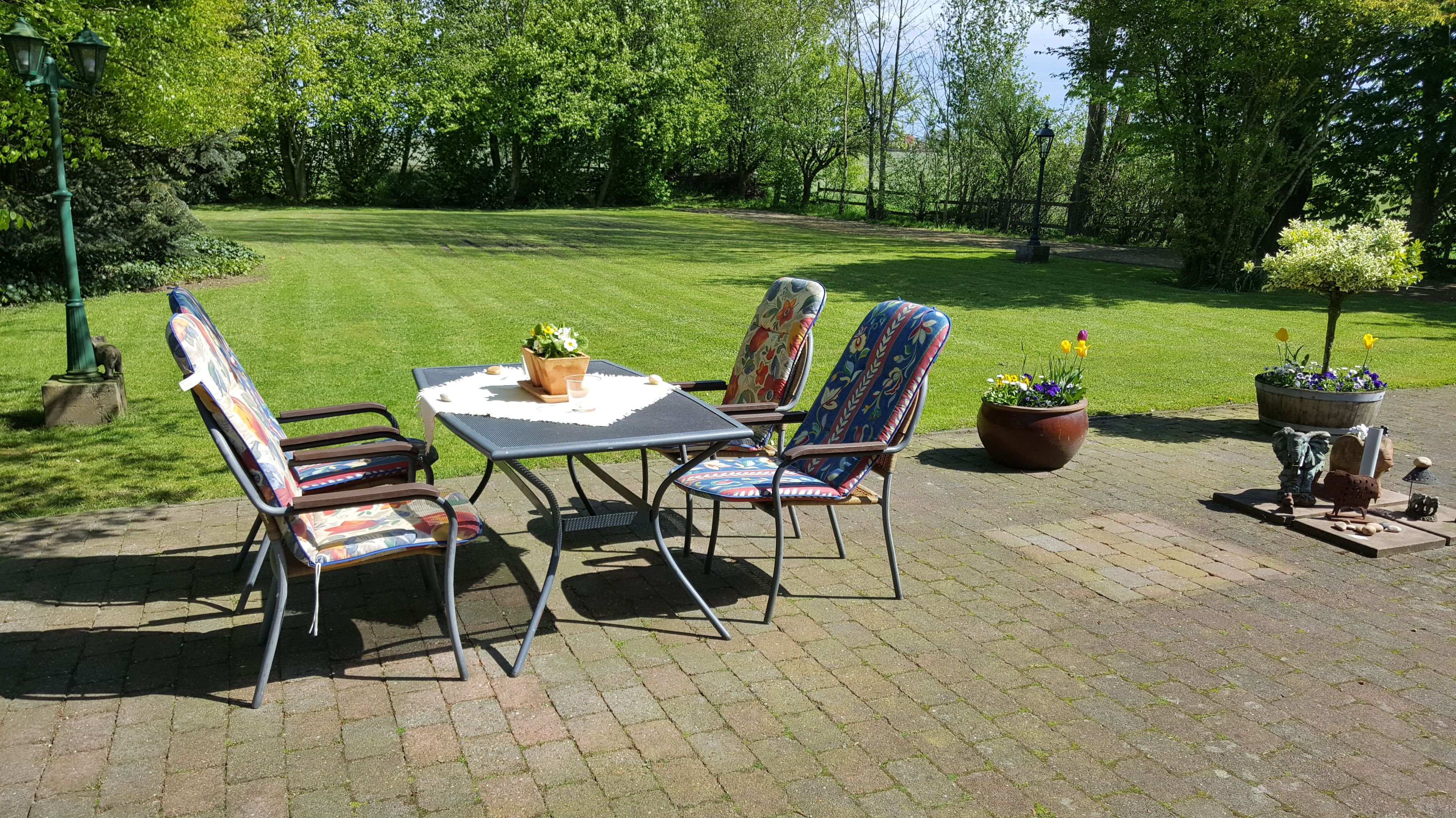 A patio with a table and chairs, surrounded by greenery and a lawn.