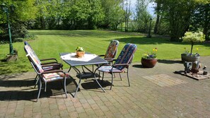 Eine Terrasse mit Tisch und Stühlen, umgeben von Grünpflanzen und einem Rasen.