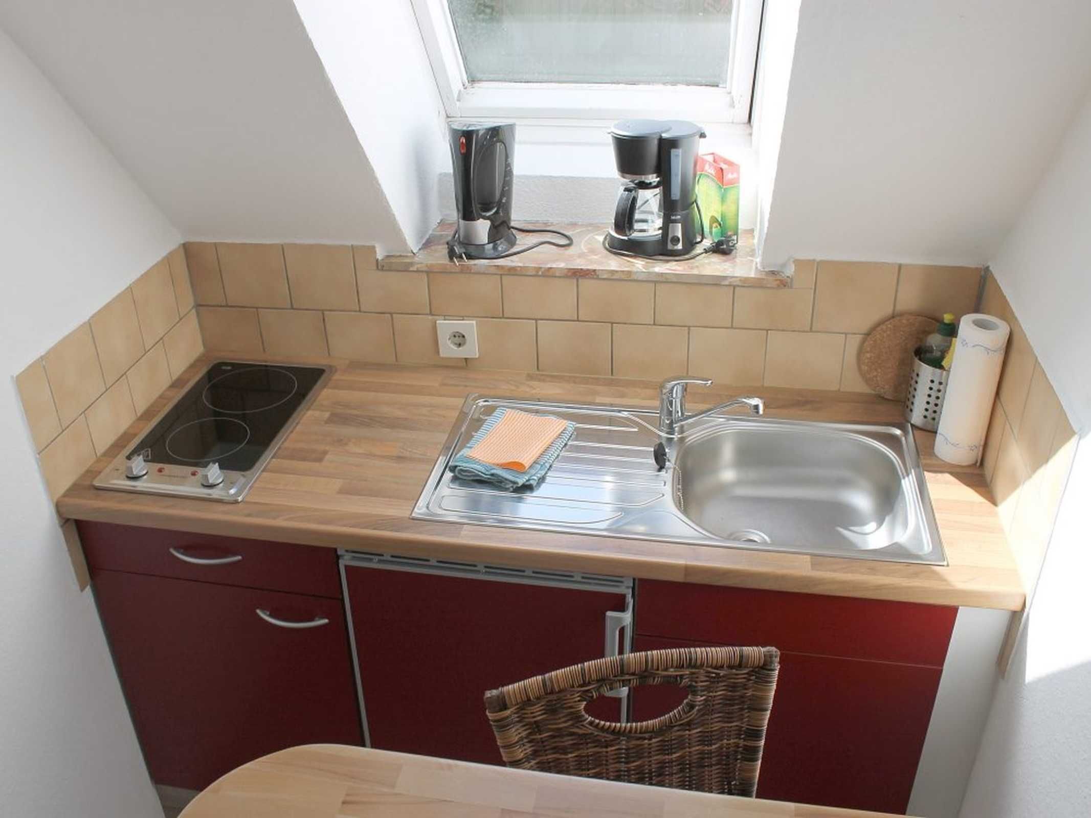 A compact kitchen with a stove, sink, and a window above the counter.