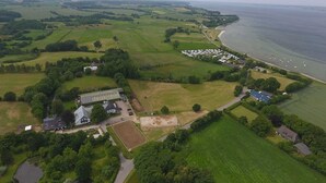 Luchtbeeld van een landgoed aan de kust, met groene velden, een groot gebouw en een strand met boten.