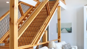 A staircase with wooden railings and a ceiling fan, leading to an upper level. A row of white sofas with patterned cushions is visible below. - Douglas Lake Retreat Private Dock + Boat (Sevierville)