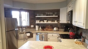 A modern kitchen with stainless steel appliances, white cabinetry, and a wooden accent wall.