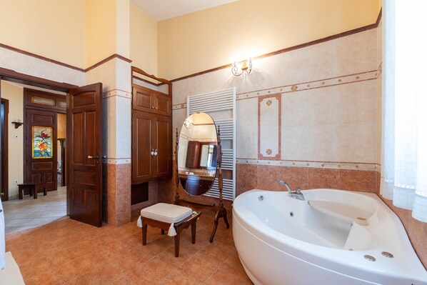Un baño con una bañera grande, armarios de madera, un banco y un espejo.