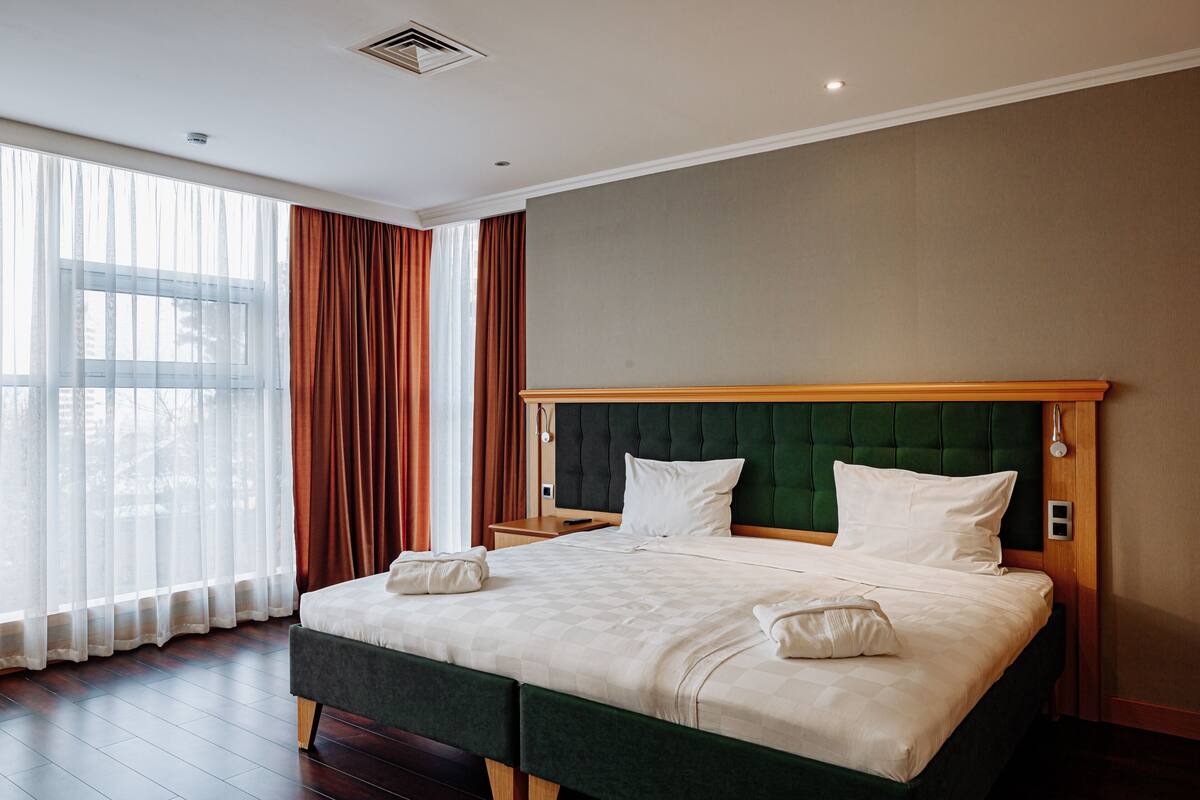 Une chambre d’hôtel avec un grand lit, une tête de lit en bois et une fenêtre avec des rideaux.