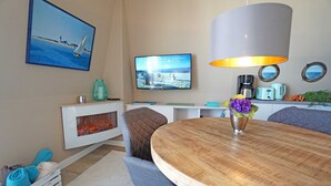 Un espace repas moderne avec une table en bois, des chaises à revêtement gris, un téléviseur fixé au mur et une cheminée en dessous.