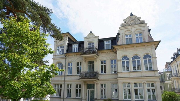 Un grand bâtiment imposant, richement décoré, doté de nombreuses fenêtres et de balcons, et entouré de verdure.