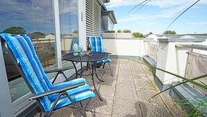 Une terrasse avec deux chaises à rayures et une table, une bouteille et un verre posés sur la table.