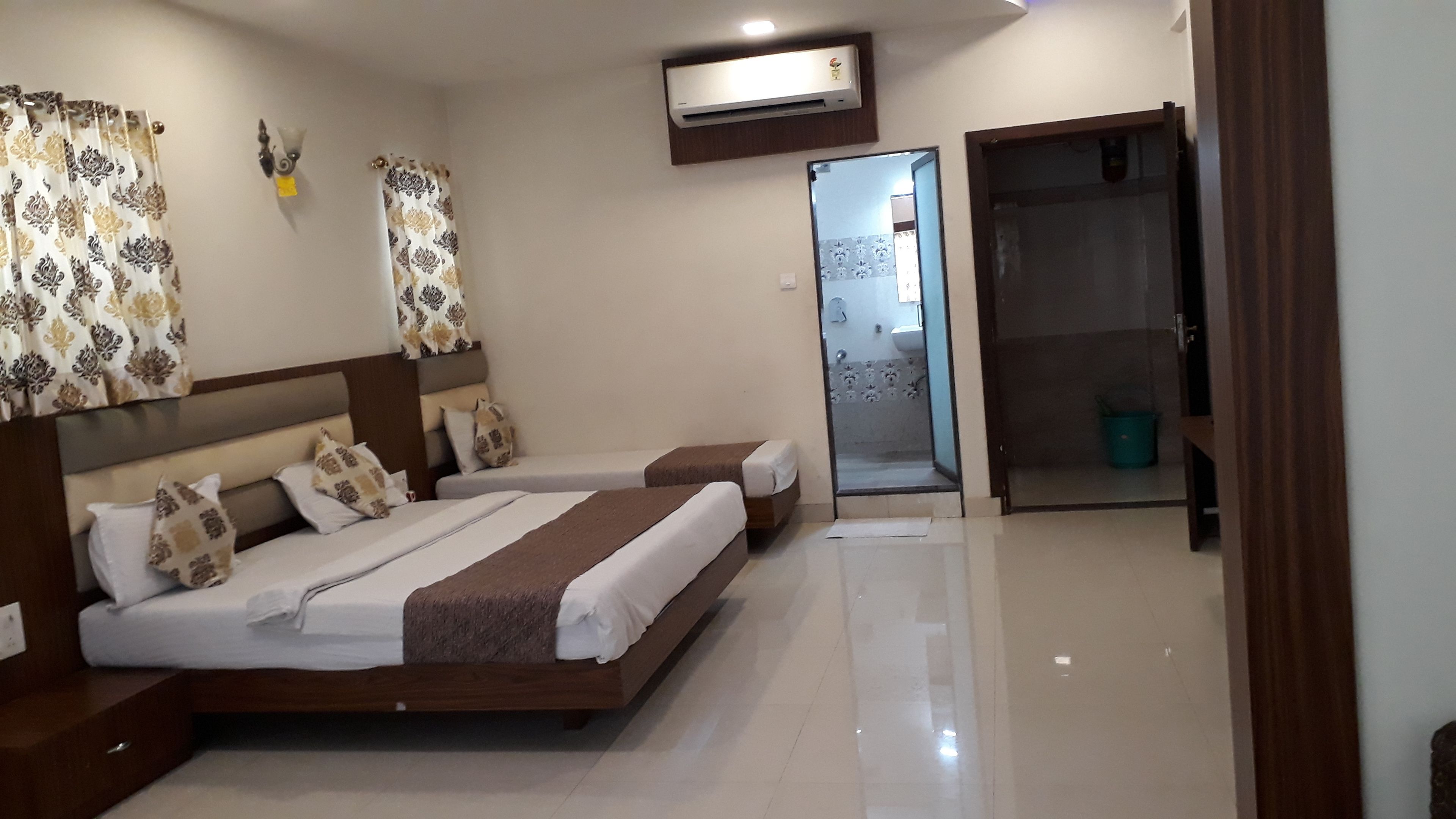 Habitación de hotel con dos camas, baño con puerta de vidrio y unidad de aire acondicionado en la pared.