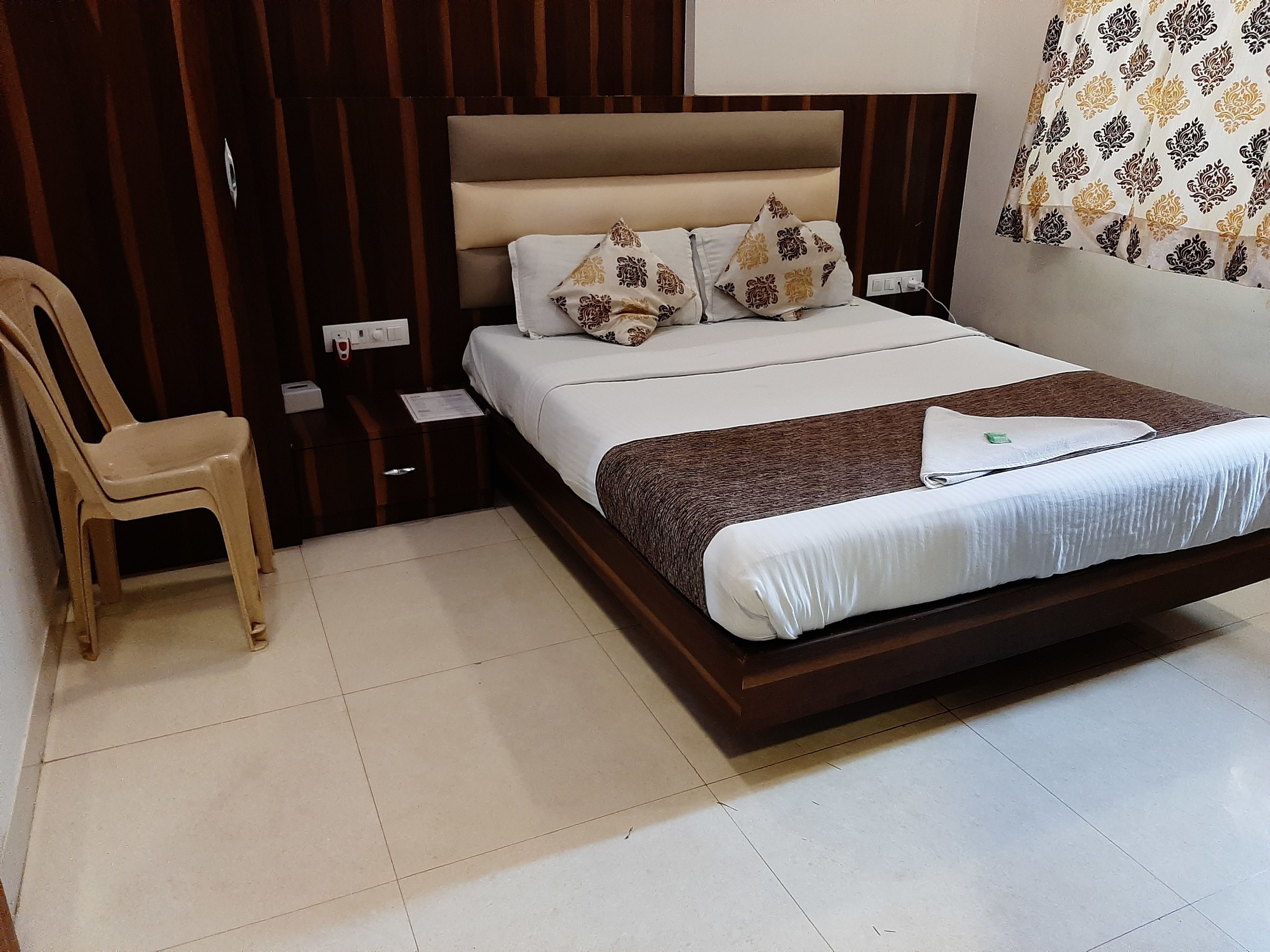 A neatly arranged bedroom with a bed, bedside table, chair, and a wall with patterned wallpaper.