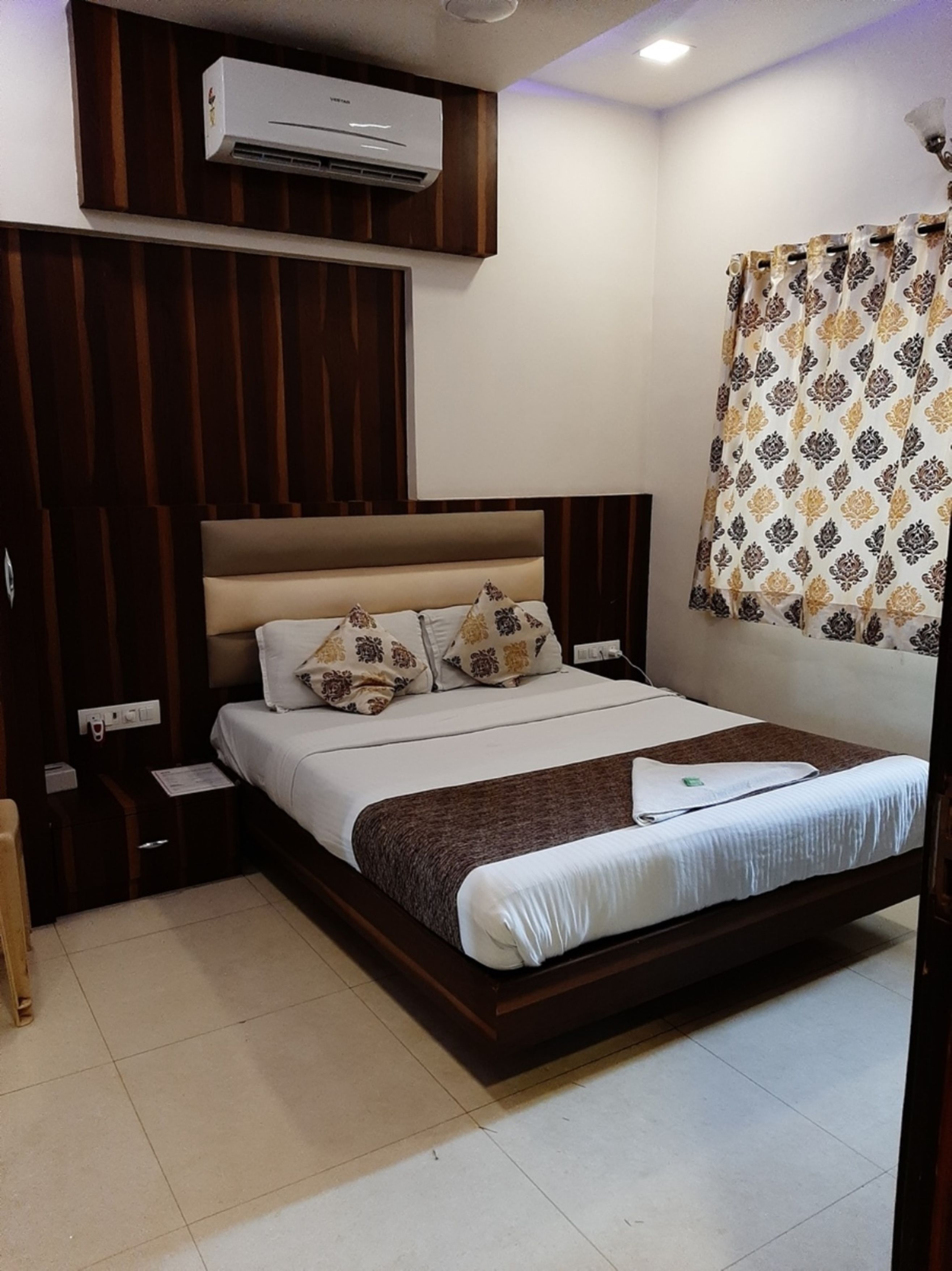 Une chambre bien rangée, avec un lit, des tables de chevet, un appareil de climatisation et un rideau.